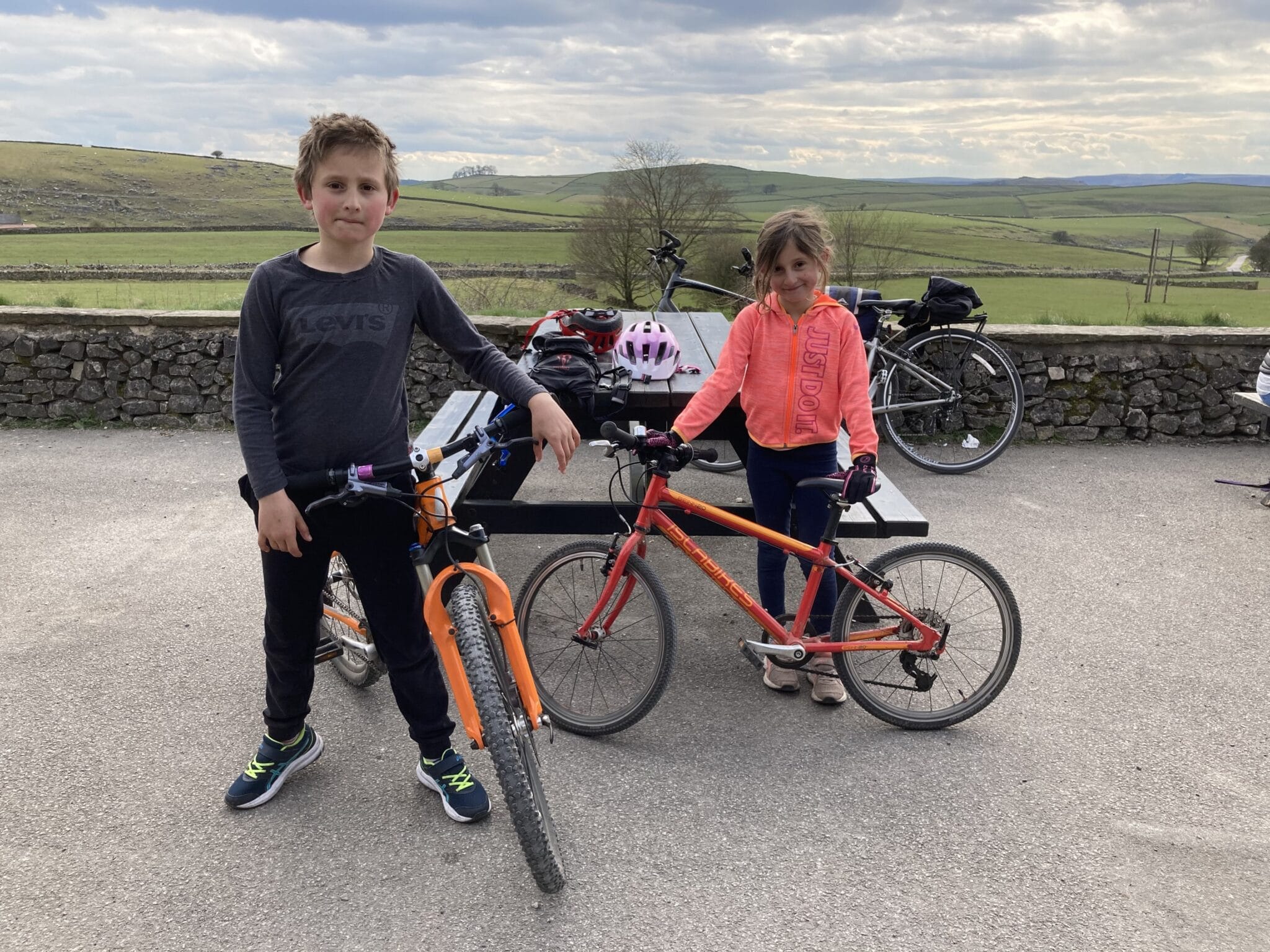 Two children standing by bicycles, in the background are rolling hills of the lake district.